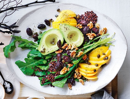 close-up view of a white plate with a vegetarian dish, including avocado and mango, greens and nuts